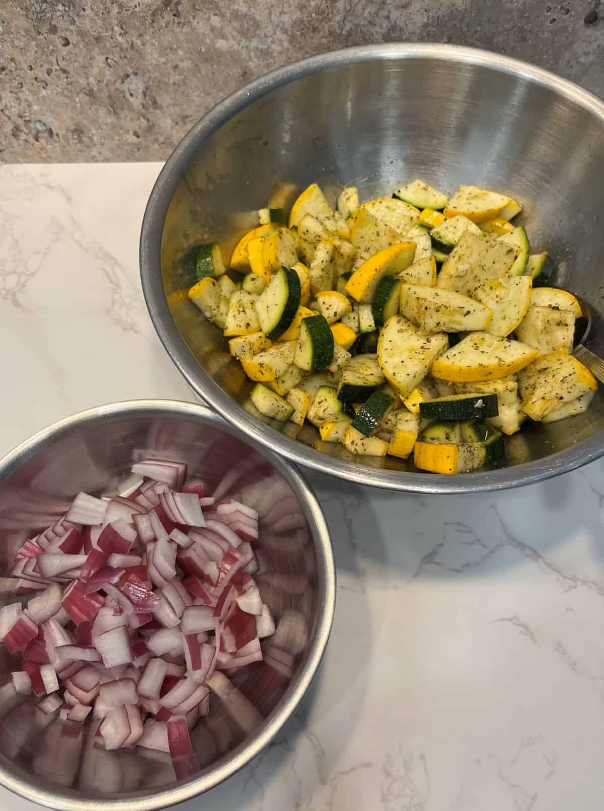 FBB_Side.Zucchini.Squash.Diced.1200x1612. A photo of seasoned zucchini and yellow squash in one bowl and and diced red onion in another bowl.