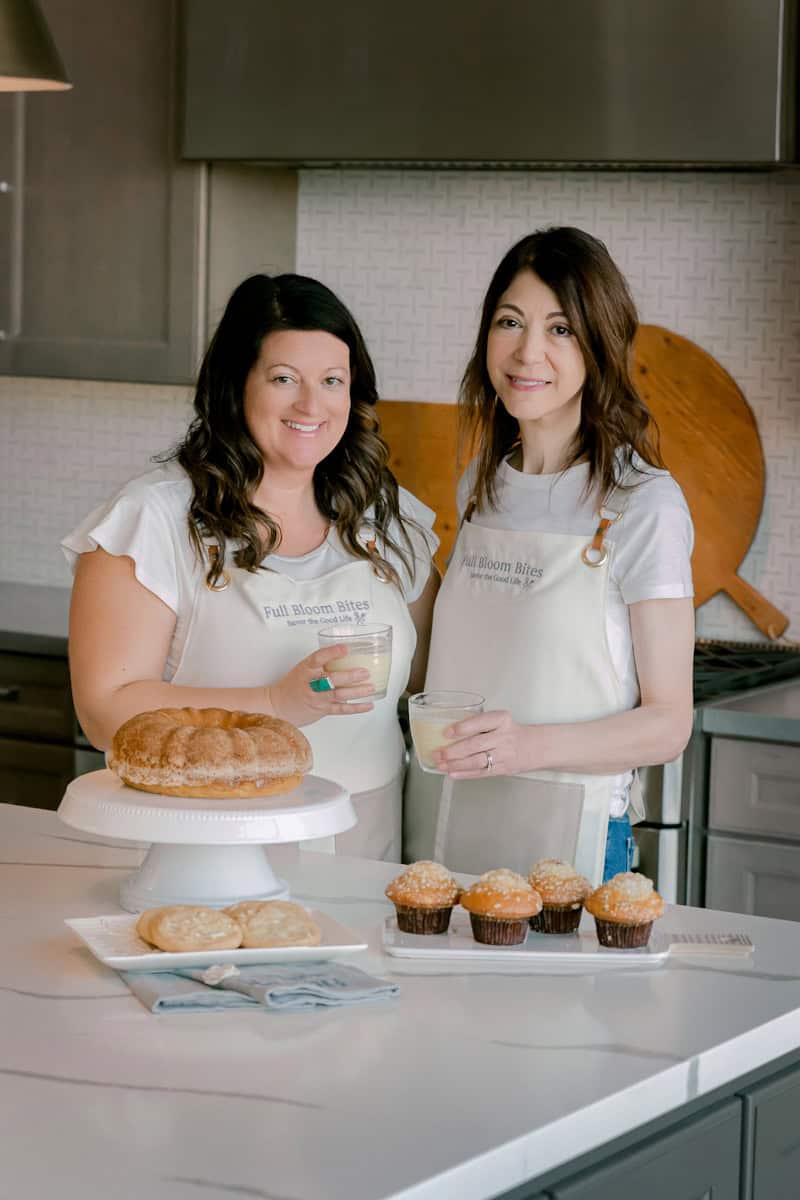 FBB_Team.Cheers_2024. Jen & Sam are in the kitchen cheering Will's version of a Mango Lassi to the good life with yummy baked goods on display.