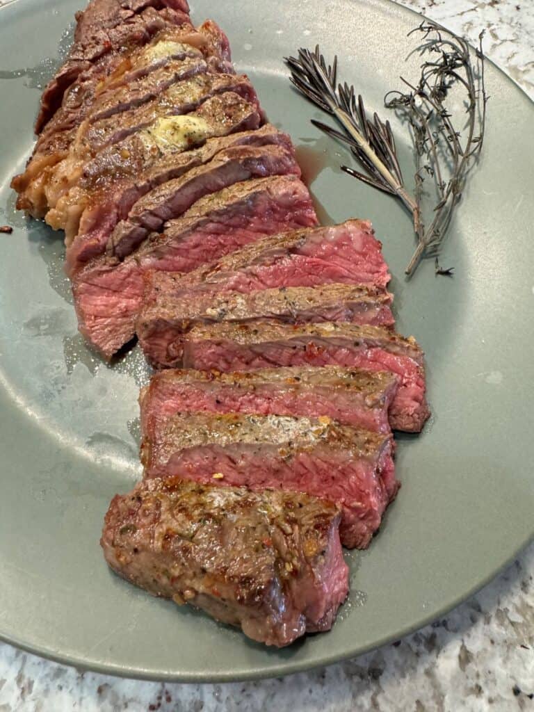 A cut medium rare rib-eye steak fanned out on a green plate with a spring of rosemary.