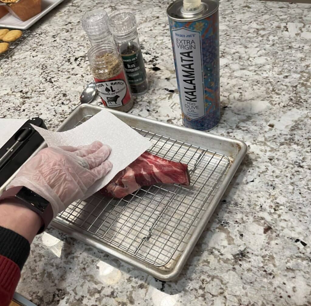 Bone-in ribeye steak being patted dry with paper towels to remove moisture after dry brining, ready for seasoning