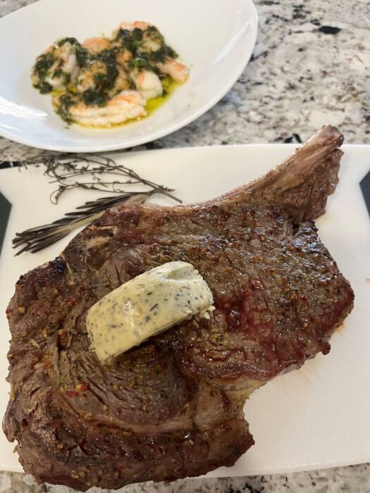 Juicy Baked Bone-In Ribeye Steak on a platter with herbed butter. 