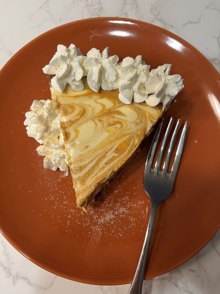 Pumpkin pie swirl cheesecake with walnut crust slice garnished with whipped cream and sugar, served with fork