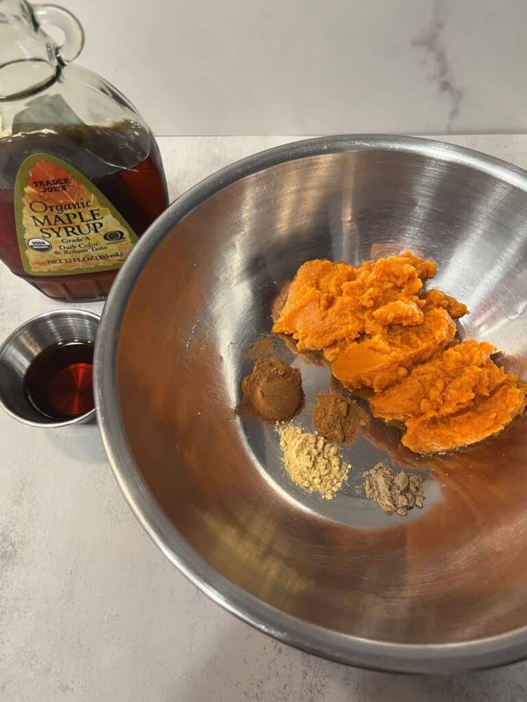 Pumpkin puree in a mixing bowl with cinnamon, ginger, nutmeg, cloves, and maple syrup ready to blend.