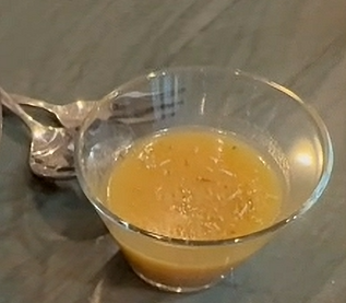 Golden honey‑dijon vinaigrette in a glass bowl on a wooden surface with a spoon beside it.