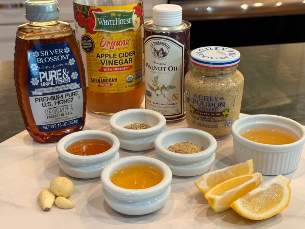 Ingredients for homemade honey‑dijon vinaigrette arranged on a light surface, including oils, mustard, honey, vinegar, and seasonings.