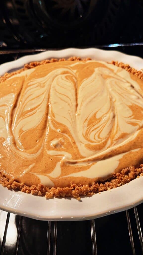 Swirled pumpkin and cream cheese pie in a white ceramic dish baking in the oven.