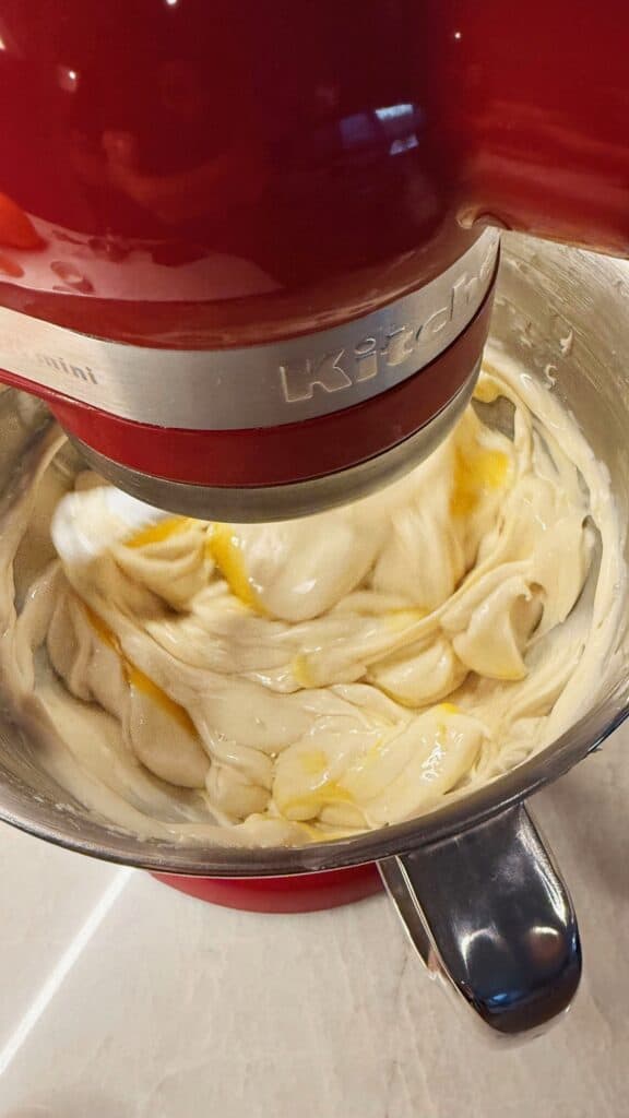 Cream cheese mixture in a stand mixer with eggs being blended in, one at a time.