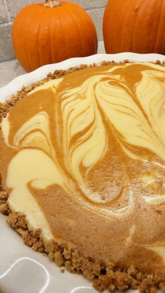 Baked pumpkin and cream cheese swirl pie in a white ceramic dish with a crumbly crust and marbled top.