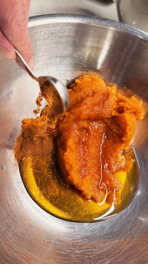 Pumpkin puree with syrup and spices in a metal mixing bowl, ready to be mixed for fall baking.