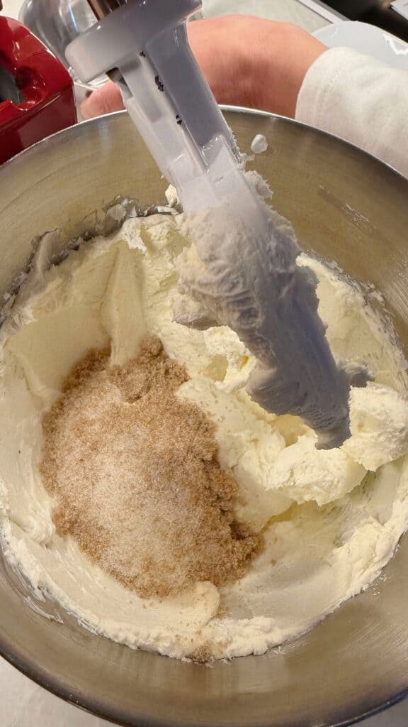 White and brown sugar layered over creamed butter in a stand mixer bowl with paddle attachment, mid-mix.