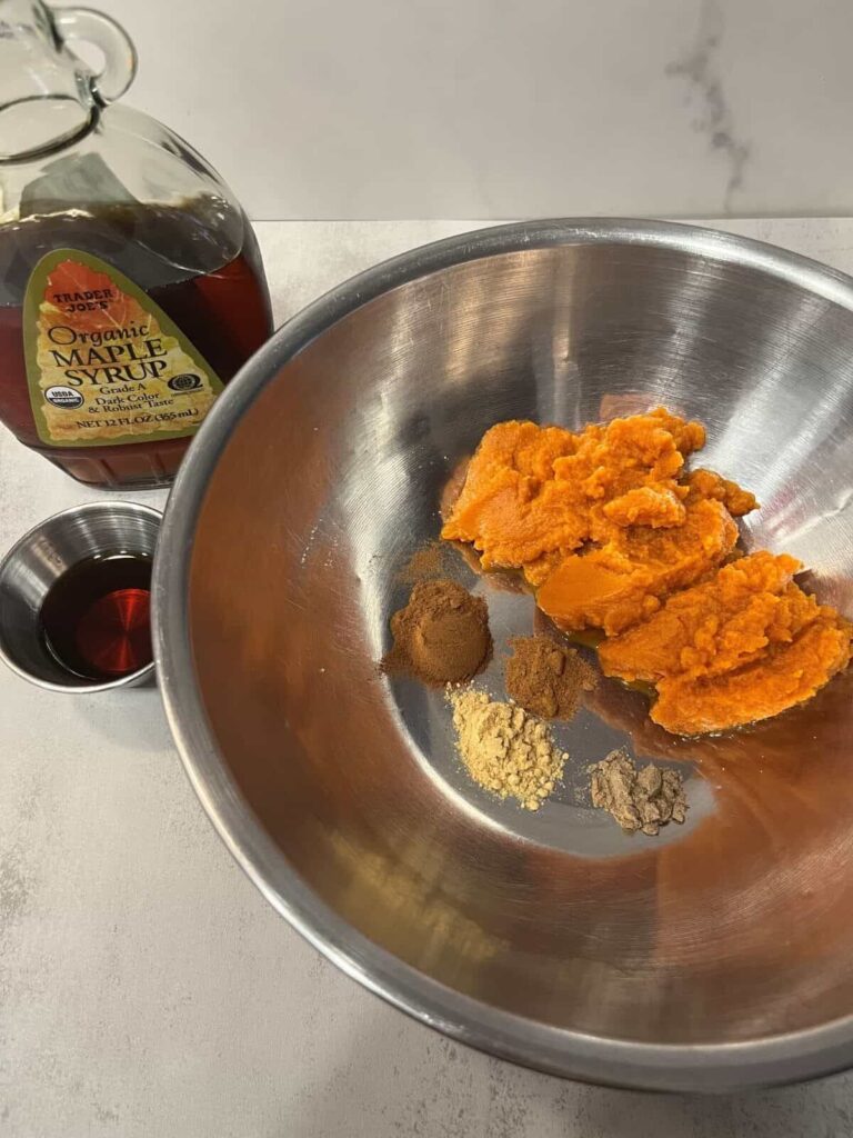 Pumpkin puree in a mixing bowl with cinnamon, ginger, nutmeg, cloves, and maple syrup ready to blend.