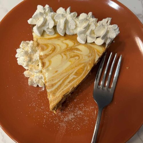 Pumpkin pie swirl cheesecake with walnut crust slice garnished with whipped cream and sugar, served with fork