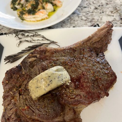 Juicy Baked Bone-In Ribeye Steak on a platter with herbed butter.