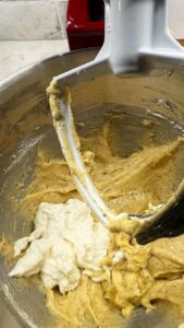 Partially mixed wet and flour batter with visible ricotta cheese rotation in a stand mixer bowl.