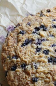 A full blueberry ricotta crumb cake cools on parchment paper, showing a golden crumb and baked‑in blueberries.