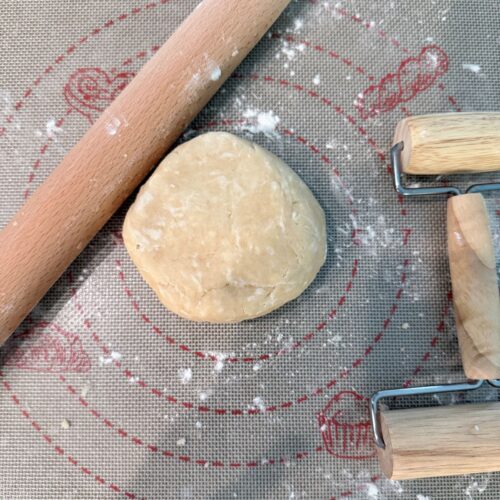 Ball of pie dough on a floured baking matt between a small and longer rolling pins.
