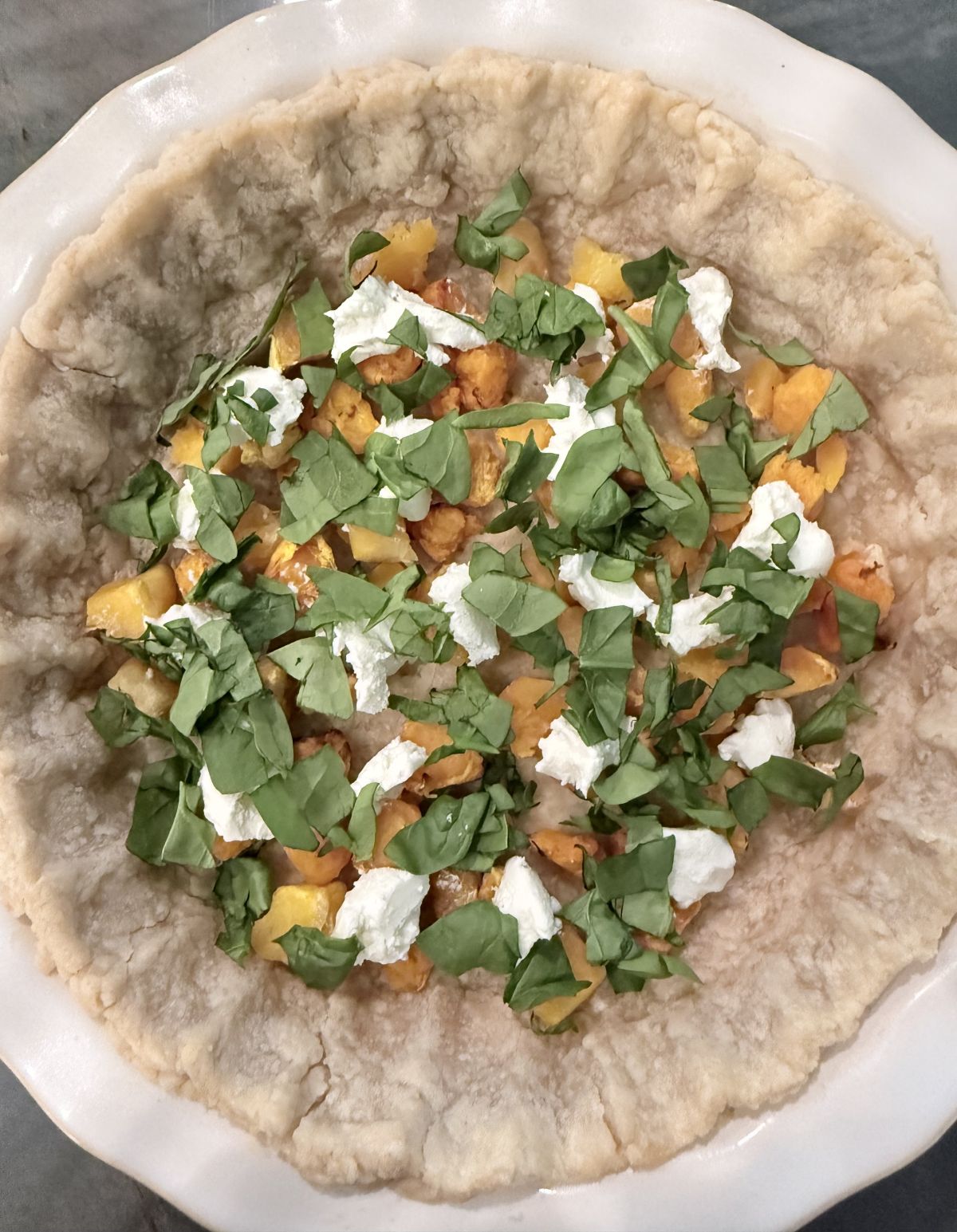 Unbaked quiche filling with chopped vegetables and herbs sitting inside a blind-bake pie crust.