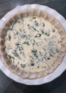 unbaked quiche showing egg-cream custard and spinach filling inside a blind-baked pie crust.