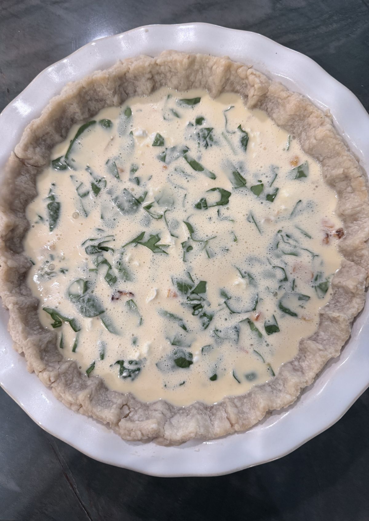 unbaked quiche showing egg-cream custard and spinach filling inside a blind-baked pie crust.