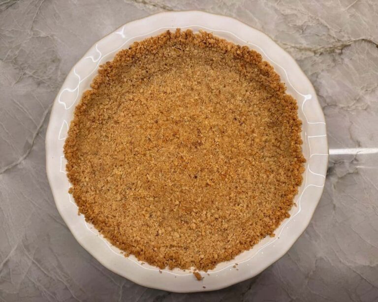 Homemade walnut pie crust in white ceramic 9-inch pie plate on kitchen counter