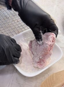 Raw chicken pieces coated in flour and resting on a paper liner during the dredging step.