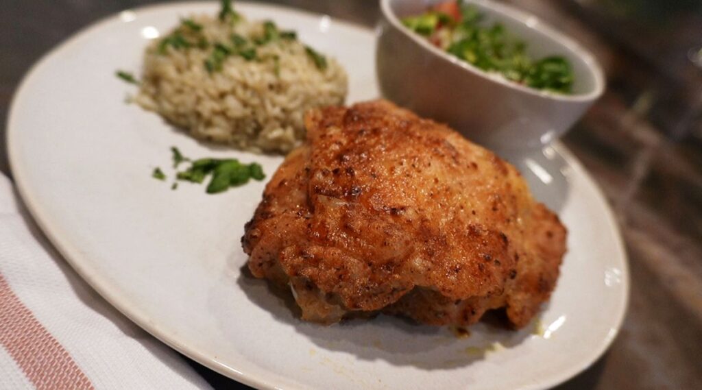 A plated meal with air fryer fried chicken, herbed rice, and a small bowl of fresh mixed salad with diced vegetables.