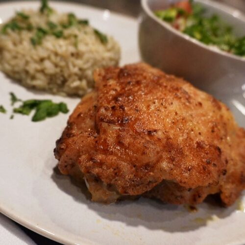 A plated meal with air fryer fried chicken, herbed rice, and a small bowl of fresh mixed salad with diced vegetables.