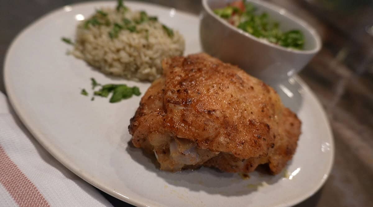A plated meal with air fryer fried chicken, herbed rice, and a small bowl of fresh mixed salad with diced vegetables.