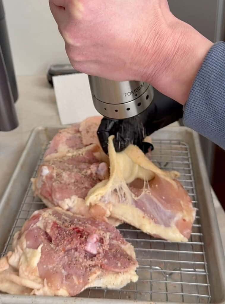 Close‑up of seasoning raw chicken pieces on a wire rack, lifting the skin to apply spices evenly.