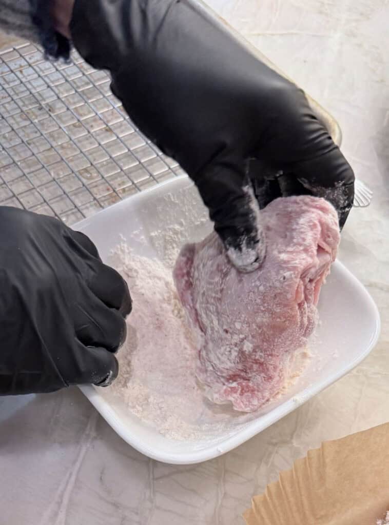Raw chicken pieces coated in flour and resting on a paper liner during the dredging step.
