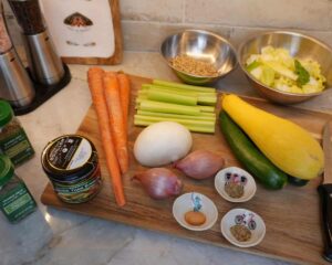 Fresh vegetables, grains, and seasonings arranged on a kitchen counter for soup preparation.