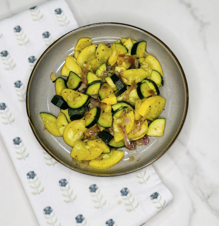 Plate of sautéed zucchini, yellow squash, and red onion served with a fork on a white cloth.