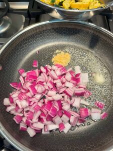 Red onions and garlic sautéing together in a frying pan during step 3 of the recipe.