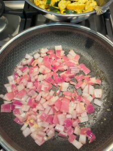Red onion and minced garlic sautéing together in a frying pan until fragrant.