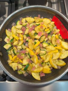 Sautéed zucchini, yellow squash, red onion, and garlic cooking in a frying pan until tender- do not over cook it.