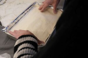 Placing the top sheets of phyllo dough over the sugared walnut filling to finish assembling baklava.