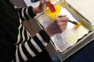 A close-up of melted ghee being brushed across the bottom and up the sides of a 9×13 baking pan.
