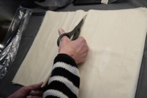 Cutting phyllo sheets with scissors to fit a 9×13 pan for baklava.