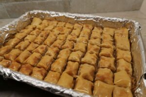 Tray of freshly baked baklava in a 9x13 pan, cut in squares, and the top is glistening with orange blossom water syrup.
