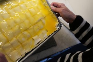 Spreading warm clarified butter (ghee) over assembled baklava before baking.