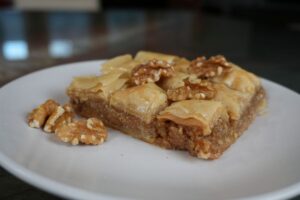 Pieces of baklava on a white plate, topped with walnuts and layered with golden, flaky filo pastry.