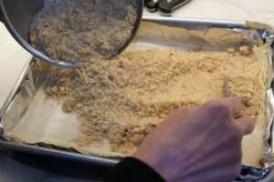 Spreading ground sugared walnuts evenly over layered phyllo for baklava filling.
