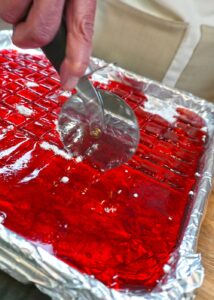 Cutting bright red cinnamon holiday hard candy into squares with a pizza cutter.