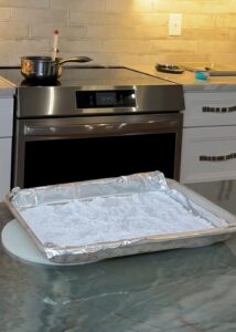 Foil‑lined baking tray coated with a layer of confectioners’ sugar, prepared for pouring hot hard‑candy syrup.