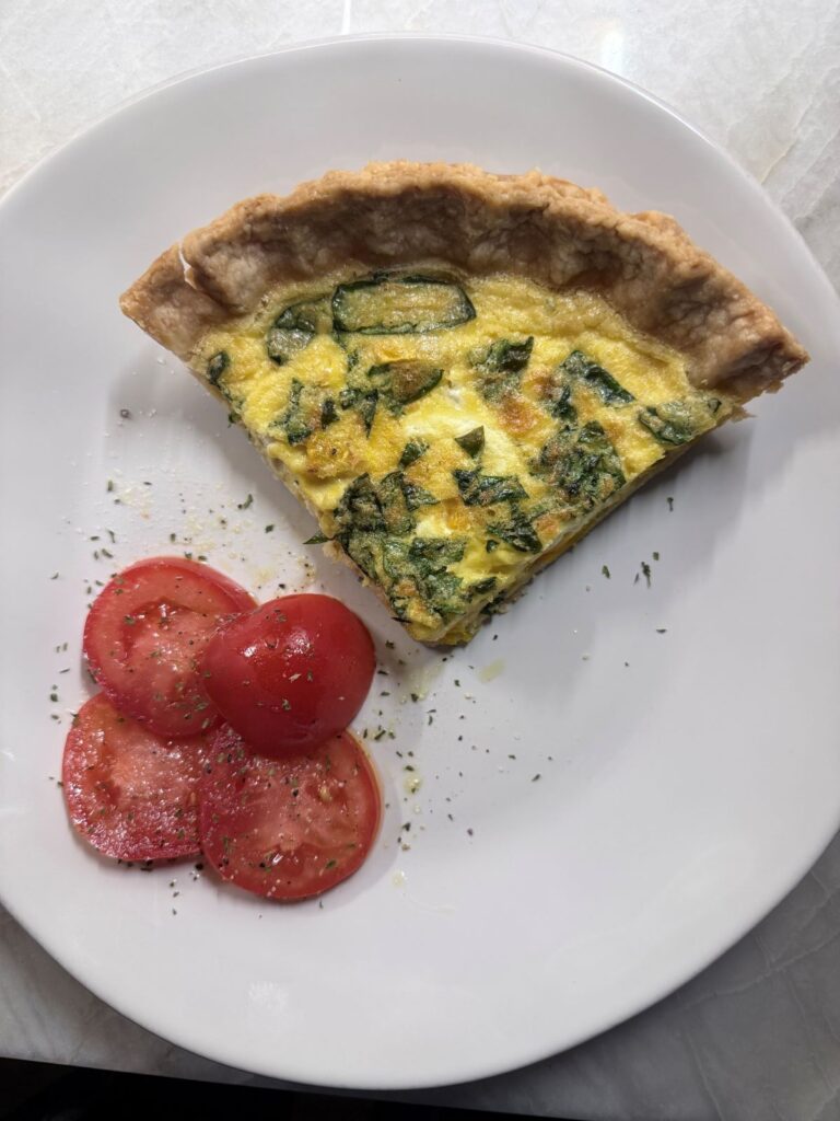 Slice of baked quiche on a white plate with fresh tomato slices.