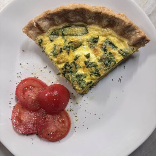 Slice of baked quiche on a white plate with fresh tomato slices.