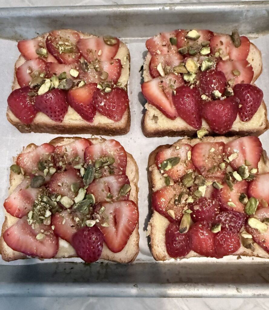 Four slices of Strawberry Almond Croissant Toast topped with crushed pistachios on a half‑sheet tray ready to be baked.