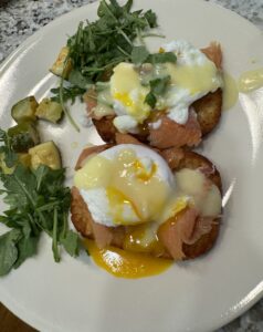 Eggs Benedict with lox served on crispy hashbrowns with hollandaise and a fresh side salad on a plate.