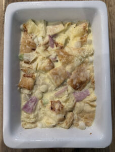 Egg custard soaking into croissant pieces in a small baking dish.
