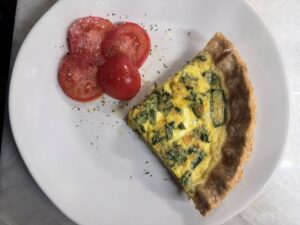 Slice of baked quiche on a white plate with fresh tomato slices.